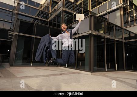 uomo d'affari felice riuscito che salta con il portatile che celebra il successo di affari all'aperto, successo Foto Stock