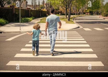 vista posteriore. padre e figlio camminano sulla zebra traversata. valore della famiglia. genitore che guida il bambino piccolo Foto Stock