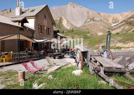 Historic Refuge Napoleon inn dal 1858 con terrazza al col de l Izoard, storico carro trainato da cavalli sulla destra, erodendo le montagne sopra la linea di alberi in Foto Stock