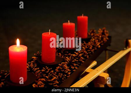 Quattro candele di Avvento decorate con coni di pino su una slitta, primo Avvento una candela che brucia Foto Stock
