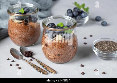 Budino di chia al cioccolato con mirtillo e mandorle in vasetti di vetro su sfondo grigio. Cibo sano Foto Stock