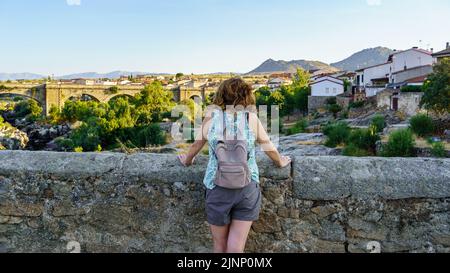 Donna turistica che domina un ponte di pietra medievale e contempla il paesaggio, Puente Congoto, Spagna. Foto Stock