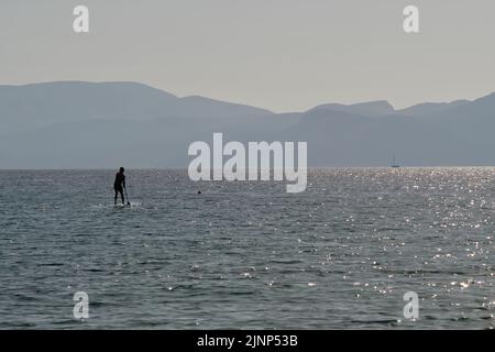 IOS, Grecia - 8 giugno 2021 : giovane turista che si diverti a fare un paddle boarding sulla famosa spiaggia di Mylopotas iOS Grecia Foto Stock