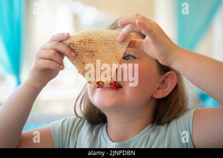 Una giovane ragazza con le trecce sta mangiando un pezzo di pizza. Foto di alta qualità Foto Stock