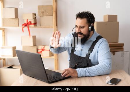 uomo d'affari indiano bearded che ha videochiamata in linea con i clienti sul laptop, indossando le cuffie . Uomo millenario concentrato che dà lezioni online Foto Stock