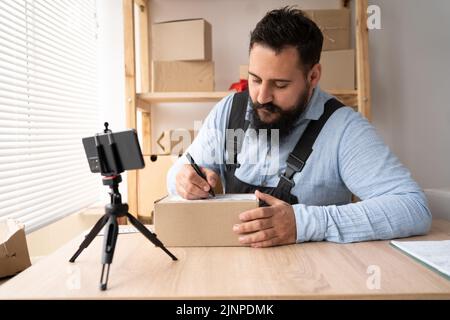 Imprenditore piccola impresa SME uomo indiano lavoro da casa utilizzare smartphone per il controllo commerciale, marketing online, scatole di imballaggio, PMI venditore, e Foto Stock