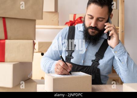 Startup indiano uomo imprenditore felice dopo il nuovo ordine dal cliente con smartphone, telefono cellulare e la scatola di consegna sul tavolo, proprietario di piccole imprese Foto Stock