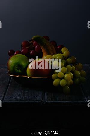 Frutta ancora vita con uva, mele e pere in antico ciotola di rame su fondo tavola di legno scuro Foto Stock