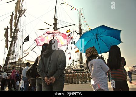 I visitatori che prestano attenzione ai cadetti della marina indonesiana che si stanno allineando per una cerimonia, sullo sfondo di KRI Dewaruci (Dewa Ruci), una nave alta indonesiana, che viene aperta ai visitatori pubblici al porto di Kolinlamil (porto della Marina) a Tanjung Priok, a nord di Giacarta, Jakarta, Indonesia. Foto Stock