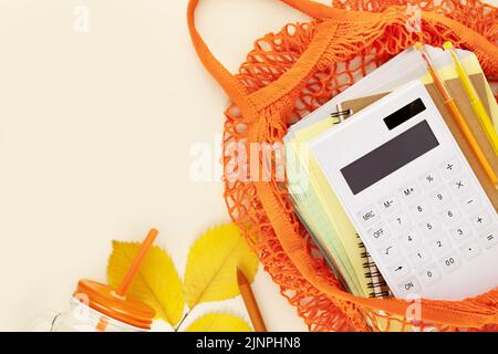 Composizione autunnale con forniture scolastiche e calcolatrice in una borsa in tessuto arancione su sfondo chiaro con foglie autunnali e spazio copia. Ritorno a scuola Foto Stock