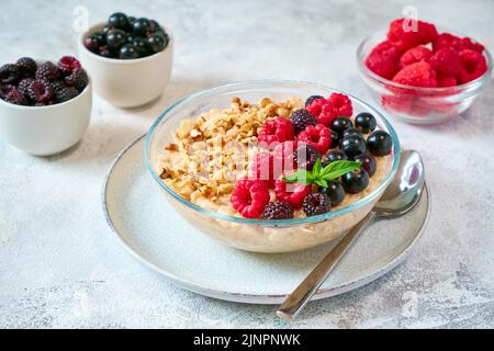 Ciotola di vetro con farina d'avena, frutti di bosco diversi e noci tritate in un ciotola di vetro. Cibo sano ed equilibrato Foto Stock