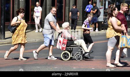 Persone, tra cui un uomo che spinge una sedia a rotelle in possesso di una donna anziana, attraversano la strada nel centro di Manchester, Regno Unito, Isole Britanniche. Foto Stock