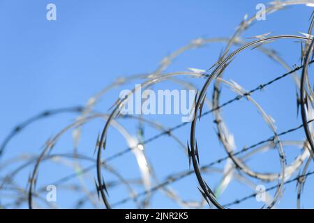 Bobine di filo rasoio su una recinzione di fissaggio contro il cielo blu con sezione più vicina a fuoco e bobine posteriori sfocate Foto Stock