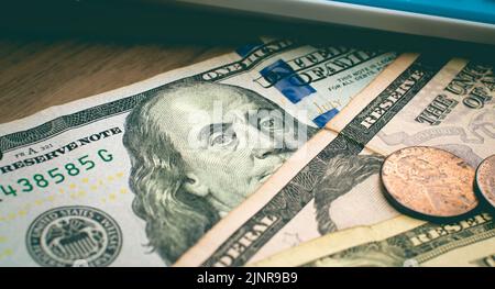 Banconote e monete IN dollari USA su un mobile di legno con una calcolatrice nella composizione. Concetti finanziari ed economici. Foto Stock