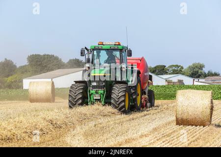 Il contadino locale guida il trattore e l'imballatrice John Dere per raccogliere e imballare il grano da tagliare per immagazzinare l'animale da lettiera e l'uso agricolo generale in inverno. N Foto Stock