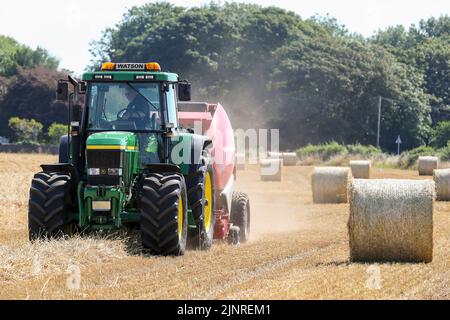 Il contadino locale guida il trattore e l'imballatrice John Dere per raccogliere e imballare il grano da tagliare per immagazzinare l'animale da lettiera e l'uso agricolo generale in inverno. N Foto Stock