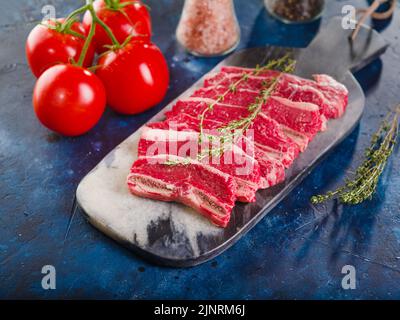 preparato per cucinare bistecche crude di manzo, maiale su un tagliere di legno su sfondo di marmo blu. Vista ad angolo basso. Libro di ricette, blog di cibo, restaur Foto Stock