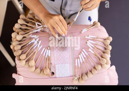 lavorazione a mano di pizzo a bobina. Le mani delle donne intrecciano i fili per fare un modello. Foto Stock