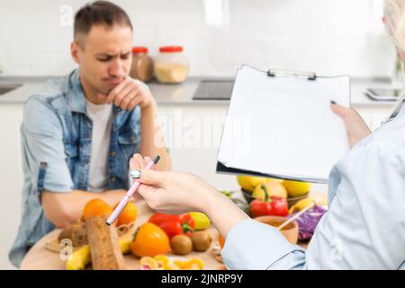 Un nutrizionista sorridente consiglia a un paziente un'alimentazione e un'alimentazione adeguate. Il medico mostra uno schema di perdita di peso senza un effetto negativo sulla salute Foto Stock