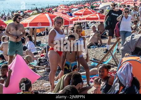 Brighton, Regno Unito. 13th ago, 2022. Migliaia di persone si sono recate a Brighton Beach questo sabato, sfruttando al meglio il caldo tempo. Un'immagine degli ombrelli rossi (sponsorizzati da Walls Ice Cream ) può essere vista allungando da Brighton lungo a Hove Credit: @Dmoonuk/Alamy Live News Foto Stock