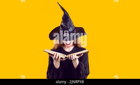 Felice giovane donna vestita come strega malvagia creepy tenere libro e leggere incantesimi magici Foto Stock