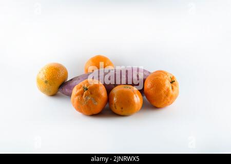 Superficie coperta con cinque tangerini freschi maturi e una patata dolce. Composizione isolata su sfondo bianco. Foto Stock