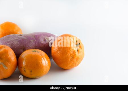 Superficie coperta con cinque tangerini freschi maturi e una patata dolce. Composizione isolata su sfondo bianco. Foto Stock