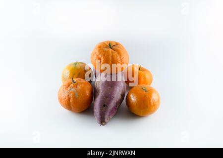 Superficie coperta con cinque tangerini freschi maturi e una patata dolce. Composizione isolata su sfondo bianco. Foto Stock