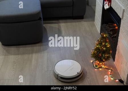 Aspirapolvere robotizzato che pulisce la stanza vicino ad un albero di Natale Foto Stock