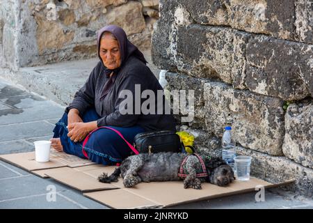 vecchia signora vestita di nero con un cane che mendicava soldi per le strade di chania sull'isola greca di creta, mendicante donna per le strade con il suo cane Foto Stock