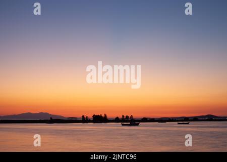 Piccola barca silhouette al crepuscolo al tramonto. Una piccola barca sull'acqua in Turchia ayvalik isola di sabbia Foto Stock