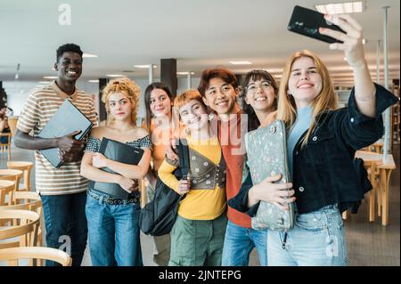 Compagni di classe multirazziali che prendono selfie in biblioteca Foto Stock