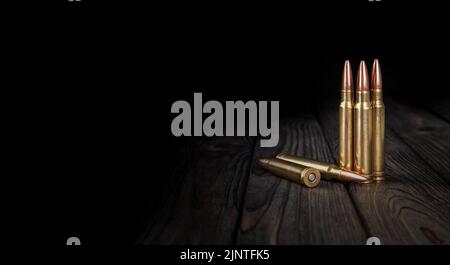 Le cartucce di carabina e fucile si trovano su una superficie di legno. Munizioni per armi. Sfondo scuro. Foto Stock