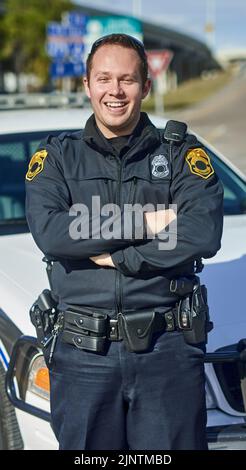 Pattugliamento delle strade. Ritratto corto di un bel giovane poliziotto in piedi con le braccia incrociate mentre fuori in pattuglia. Foto Stock