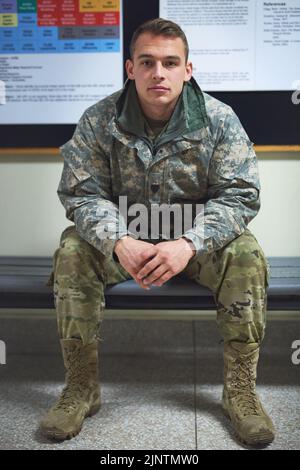 Un giovane soldato seduto su una panchina nella sala di un'accademia militare. Foto Stock