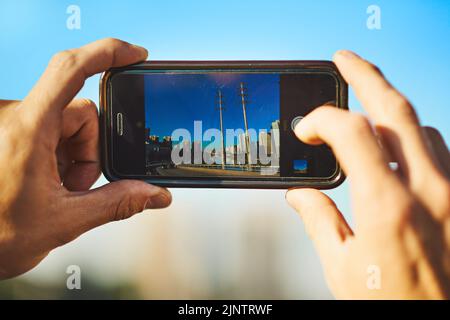 I paesaggi sono i miei preferiti da catturare. Un uomo irriconoscibile che scatta una foto della città con il suo cellulare fuori. Foto Stock