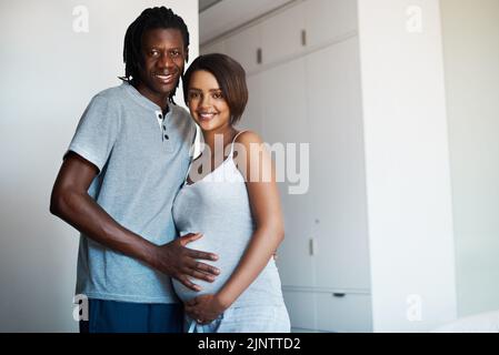 Questa gravidanza ci ha avvicinato più di prima. Ritratto di giovane felice in posa con la moglie incinta a casa. Foto Stock