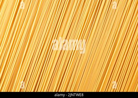 Sfondo alimentare italiano, spaghetti crudi che riempiono la cornice in un disegno testurizzato di linee diagonali di pasta. Foto Stock
