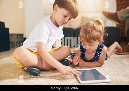 Nell'era dell'app, un adorabile fratello e una sorella che usano un tablet digitale insieme a casa. Foto Stock