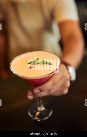Ho fatto questo specialmente per voi. Primo piano di un barman irriconoscibile che mette un cocktail sul bancone che ha appena fatto all'interno di un ristorante durante Foto Stock
