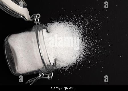 sale marino in vaso di vetro isolato su fondo nero, prodotto minerale utilizzato in cucina e cosmetici, macro foto di condimento, primo piano Foto Stock