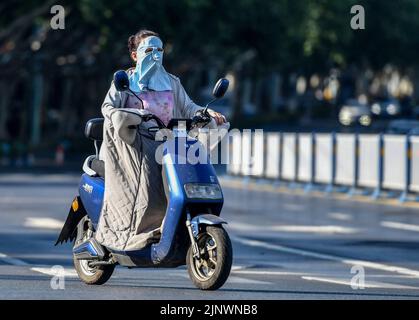 Fuyang, Cina. 14th ago, 2022. Una donna guida una bicicletta elettrica sulla sua strada come lei indossa una maschera di protezione solare verso i forti raggi ultravioletti. L'Osservatorio Meteorologico Centrale della Cina ha emesso un avvertimento rosso ad alta temperatura. Si prevede che la temperatura massima in alcune parti della Cina raggiungerà oltre i 40 ? Il 14 agosto. Credit: SOPA Images Limited/Alamy Live News Foto Stock