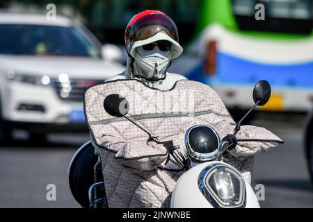 Fuyang, Cina. 14th ago, 2022. Una donna guida una bicicletta elettrica sulla strada mentre indossa una maschera di protezione solare e un casco per proteggersi dai forti raggi ultravioletti. L'Osservatorio Meteorologico Centrale della Cina ha emesso un avvertimento rosso ad alta temperatura. Si prevede che la temperatura massima in alcune parti della Cina raggiungerà oltre i 40 ? Il 14 agosto. Credit: SOPA Images Limited/Alamy Live News Foto Stock