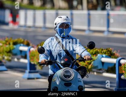 Fuyang, Cina. 14th ago, 2022. Una donna guida una bicicletta elettrica sulla strada mentre indossa una maschera di protezione solare e un casco per proteggersi dai forti raggi ultravioletti. L'Osservatorio Meteorologico Centrale della Cina ha emesso un avvertimento rosso ad alta temperatura. Si prevede che la temperatura massima in alcune parti della Cina raggiungerà oltre i 40 ? Il 14 agosto. Credit: SOPA Images Limited/Alamy Live News Foto Stock