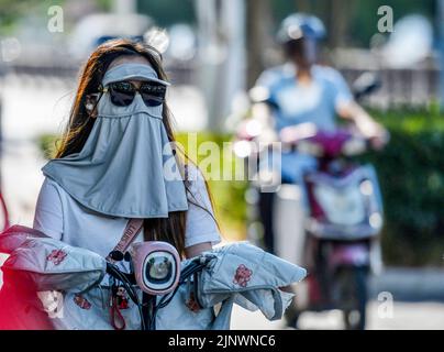 Fuyang, Cina. 14th ago, 2022. Una donna guida una bicicletta elettrica sulla strada mentre indossa una maschera di protezione solare e occhiali da sole verso i forti raggi ultravioletti. L'Osservatorio Meteorologico Centrale della Cina ha emesso un avvertimento rosso ad alta temperatura. Si prevede che la temperatura massima in alcune parti della Cina raggiungerà oltre i 40 ? Il 14 agosto. Credit: SOPA Images Limited/Alamy Live News Foto Stock