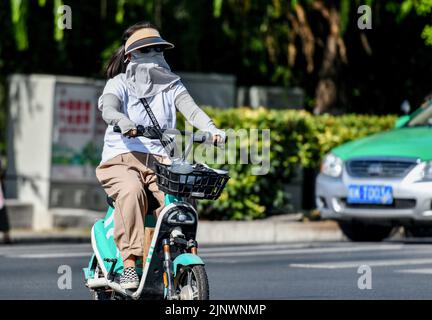 Fuyang, Cina. 14th ago, 2022. Una donna guida una bicicletta elettrica sulla strada mentre indossa una maschera di protezione solare e occhiali da sole verso i forti raggi ultravioletti. L'Osservatorio Meteorologico Centrale della Cina ha emesso un avvertimento rosso ad alta temperatura. Si prevede che la temperatura massima in alcune parti della Cina raggiungerà oltre i 40 ? Il 14 agosto. (Foto di Sheldon Cooper/SOPA Images/Sipa USA) Credit: Sipa USA/Alamy Live News Foto Stock