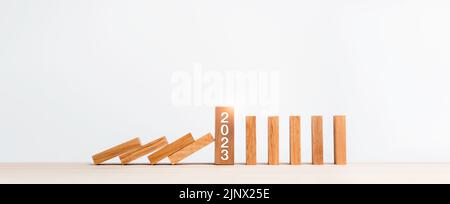 Il calendario dei numeri di 2023 anni sui blocchi di cubo di legno smette di cadere blocchi e di crollare dominali sul tavolo isolato su sfondo bianco. Prevenzione del Foto Stock