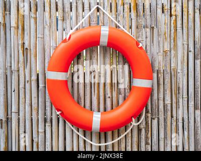 Una lifboa arancione, anello di sicurezza appeso su sfondo muro di bambù recinto, vista centrale. Attrezzatura di salvataggio. Lifesaver, concetti di sicurezza. Foto Stock