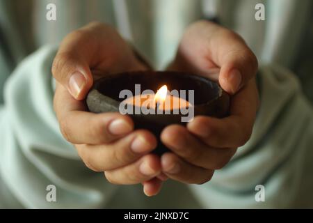 Persona che tiene in mano una candela. Ragazza junior che tiene la luce di candela in una tradizionale ciotola di ceramica in mano. Foto Stock