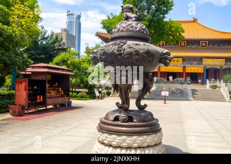 Antica scultura metallica di fronte ad un tradizionale edificio religioso Cinese. Il pezzo d'arte si trova in una piazza o plaza. Foto Stock